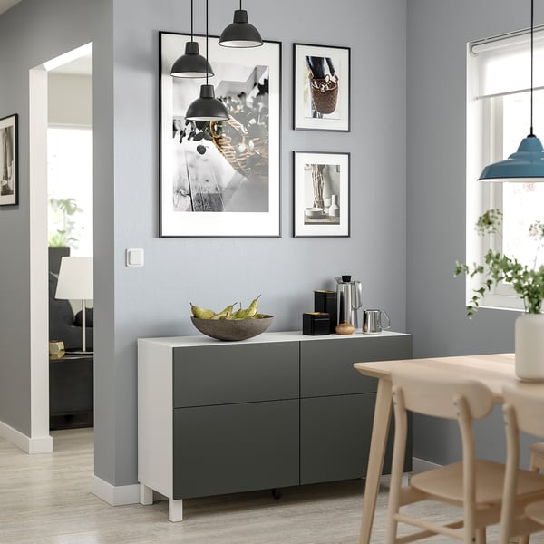 Modern living room with a white and grey sideboard, featuring black pendant lights, framed photos, and wooden chairs.