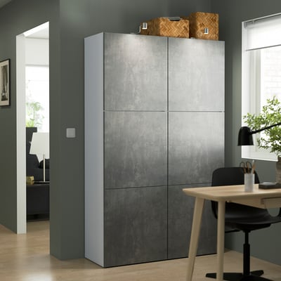 Grey BESTÅ shelving with textured doors, taller than desk & chair, blue-green wall.