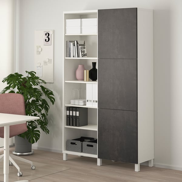 White & grey BESTÅ storage unit with open & closed compartments, near plant & chair.