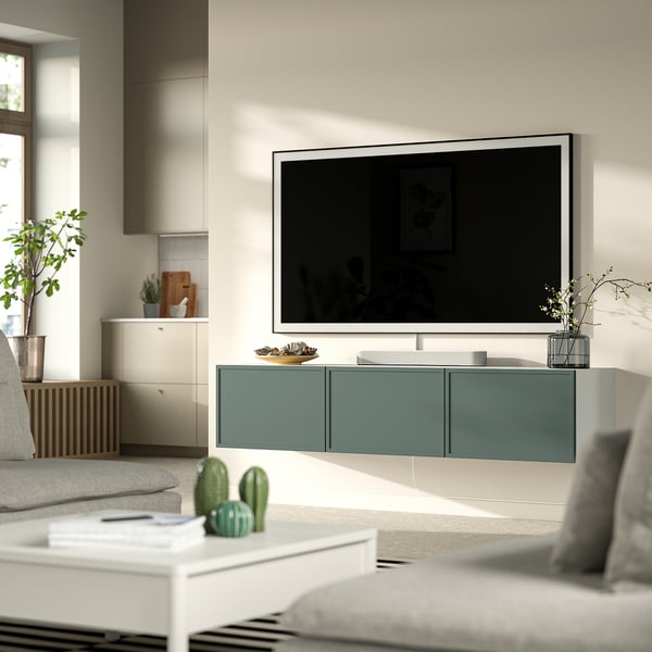 Modern living room with white sofa, large flat-screen tv on turquoise wall-mounted unit, green cactus, and coffee table with remote and coasters.