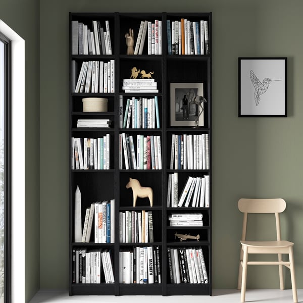 Black BILLY bookcase with books, chair, & hummingbird art against green wall.