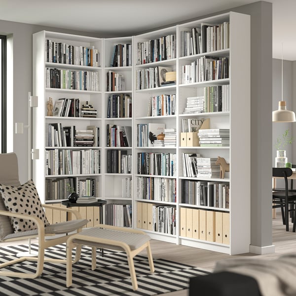 Large BILLY white bookshelf fills corner, filled with books & decor, accompanied by white chair, striped rug.