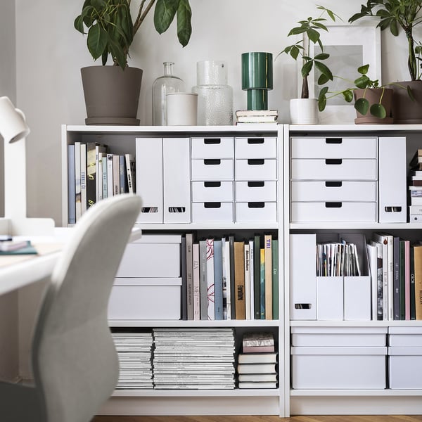 White BILLY bookshelf with drawers and shelves holding books, decor, and plants. Its larger than other items around it.