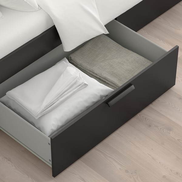 Black bed frame with open drawers, storing folded white linens and grey blanket, showcasing storage functionality.
