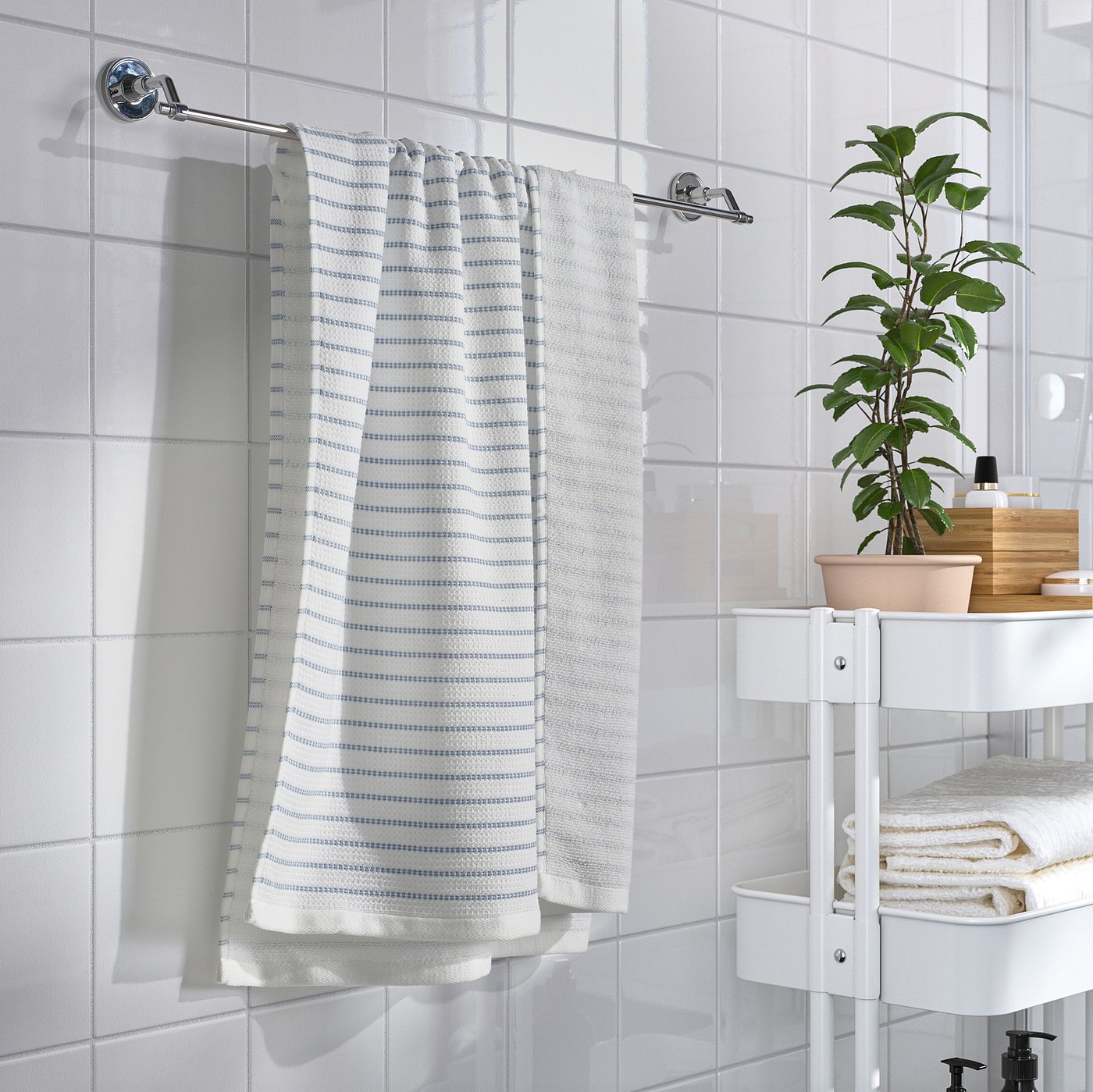 Modern bathroom with chrome BROFJÄRDEN towel rail, white towels, and a green plant on a three-tier white shelf.
