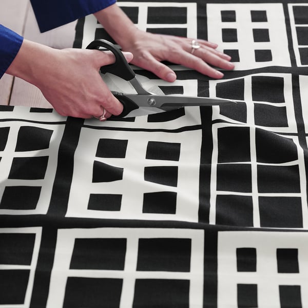 A person cuts pre-cut fabric with black and white windowpane pattern for sewing projects.