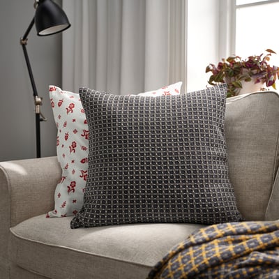 Modern living room with grey throw pillows, red floral & dark grey geometric. Grey couch, plaid blanket, tall floor lamp.