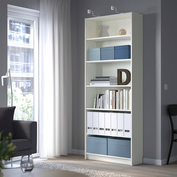 White DRÖNA storage box in bookcase. Decorative items on shelves. Chair and window in background.