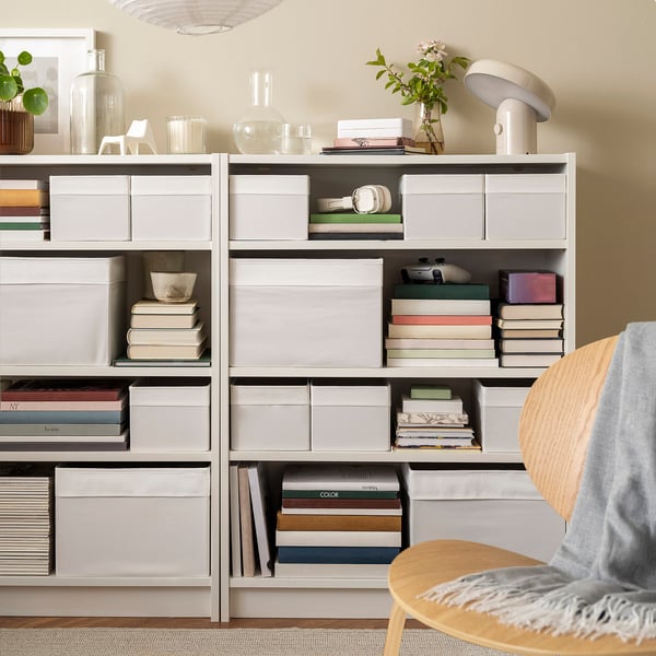 White DRÖNA boxes on grey bookcase shelves, storing books and decor, optimising space.