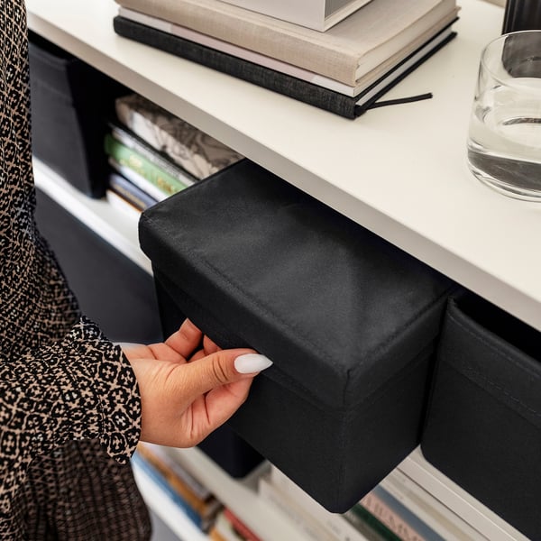 Hand pulls black fabric storage box from white shelf, ideal for organising items in limited spaces.