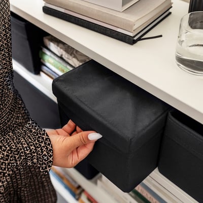 Person pulling black fabric lid off white storage box holding books.