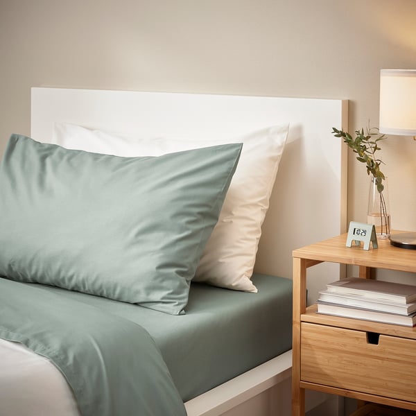 Minimalist bedroom featuring DVALA grey-green pillowcase on bed, surrounded by light-colored decor. Pillowcase size fits standard pillow.