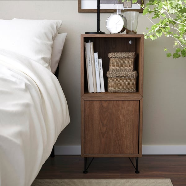 Modern brown bedside table with open & closed storage, beside bed, holds books & boxes.