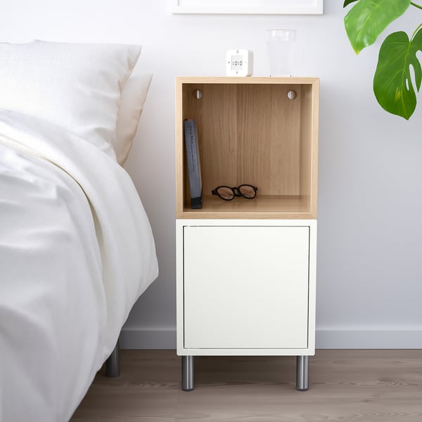 Clean, modern bedside setup with white EKET bedside table, half-open for display, half-closed for storage, next to a large bed with white linens.
