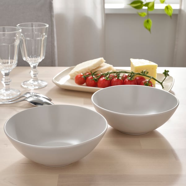 Two white bowls on a wooden table beside a plate of bread, cheese, and tomatoes.