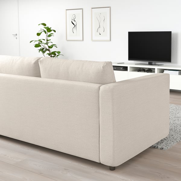 Modern beige FINNALA sectional sofa in minimalist living room, positioned against white walls, with a flat-screen tv and decorative plant.