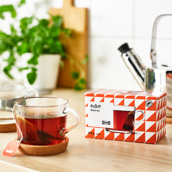 Clear mug of steaming black tea beside an opened ikea FLÖJT tea box with 25 tea bags on a wooden table, suggesting its ready to drink.