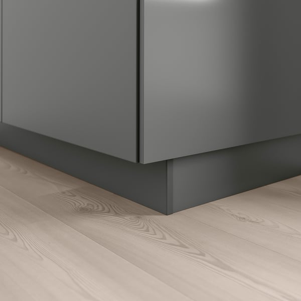 A modern kitchen plinth in dark grey, placed at the corner of a wooden floor, providing a seamless finish to base cabinets.
