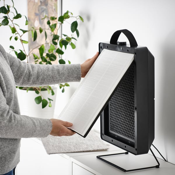 Person placing a white philtre into a black air purifier with a handle, improving indoor air quality.
