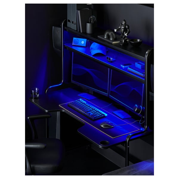 Black gaming desk, FREDDE, with blue led lights. Cup holders, adjustable shelves, and contoured tabletop. Includes keyboard, mouse, and monitor setup.