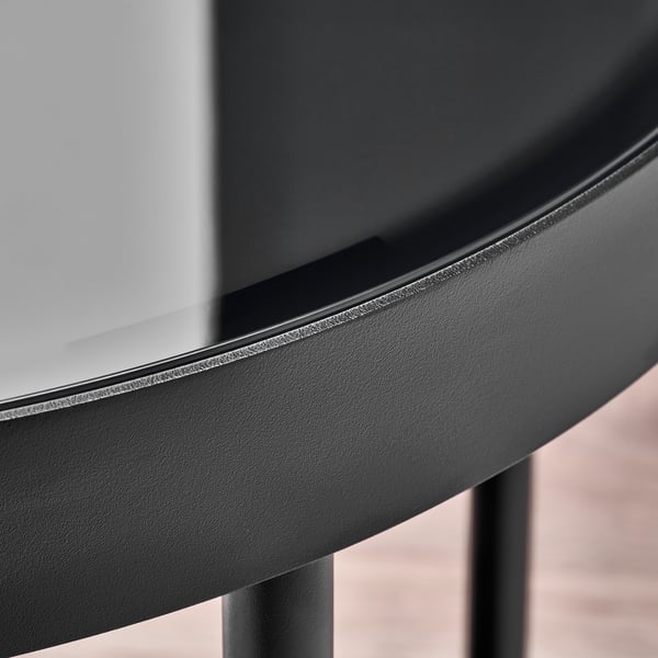 Close-up of sleek black round table edge, featuring smooth glass top and sturdy powder-coated metal legs.