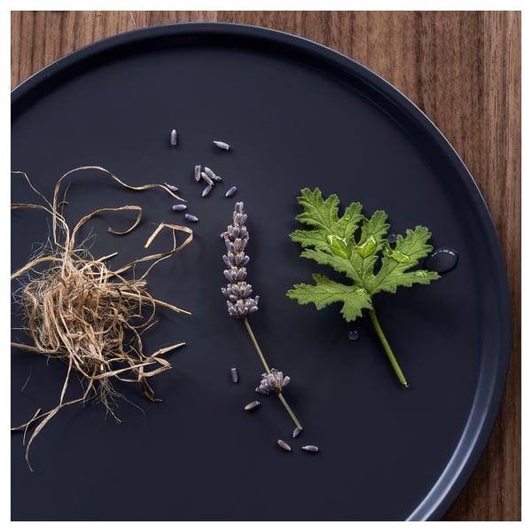 Black round tray, lavender stems, dried leaves, droplets, woodsy background.