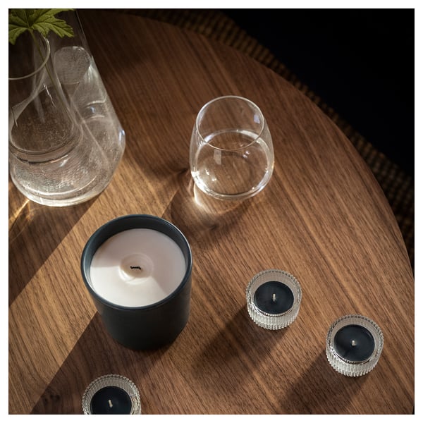 Cosy table setup: black candle, glasses, and plant in wooden bowl.
