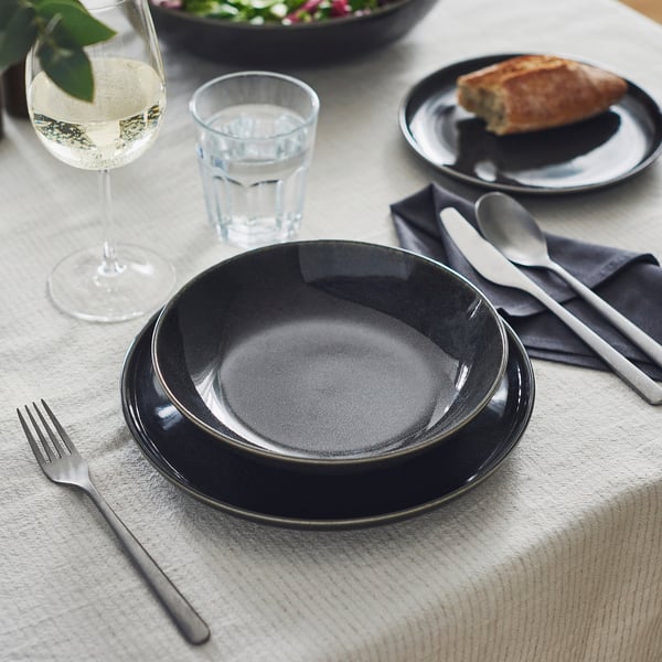 Dark grey stoneware plate for elegant table setting with cutlery, glass, and napkin.