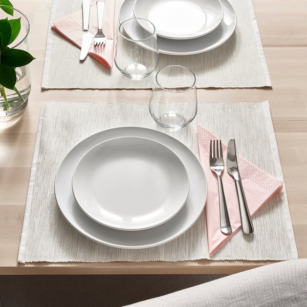 Two table settings with white plates, cutlery, glasses, and cloth napkins on placemats on a wooden table.