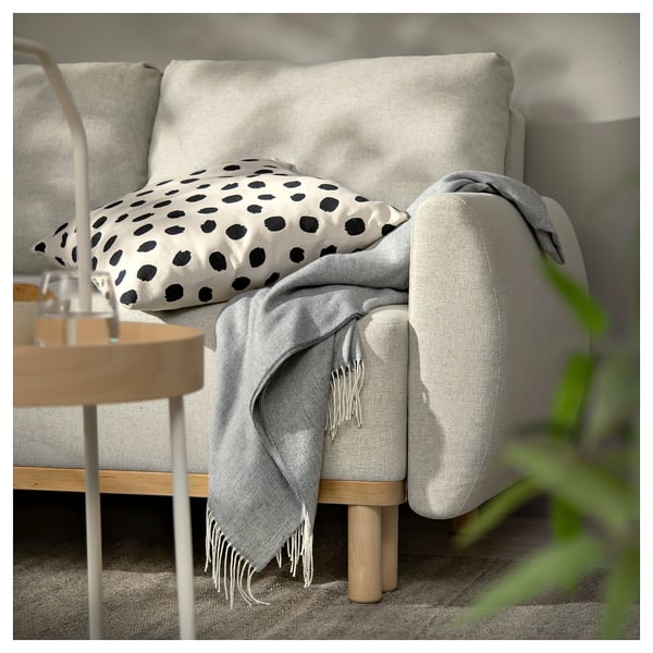 Modern grey sofa-bed with polka dot pillow and blanket, wooden legs, cosy design.