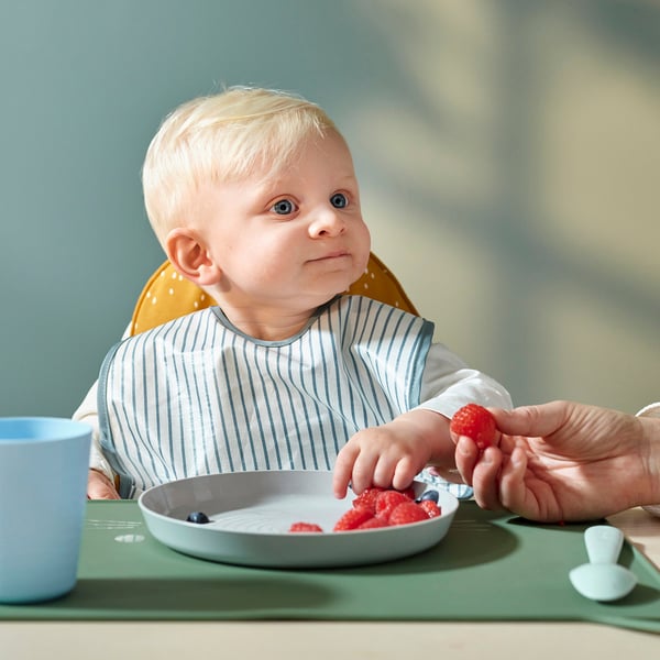 Baby eating with GULDVÄVARE bib, striped front, dotted back, adjustable neck strap.