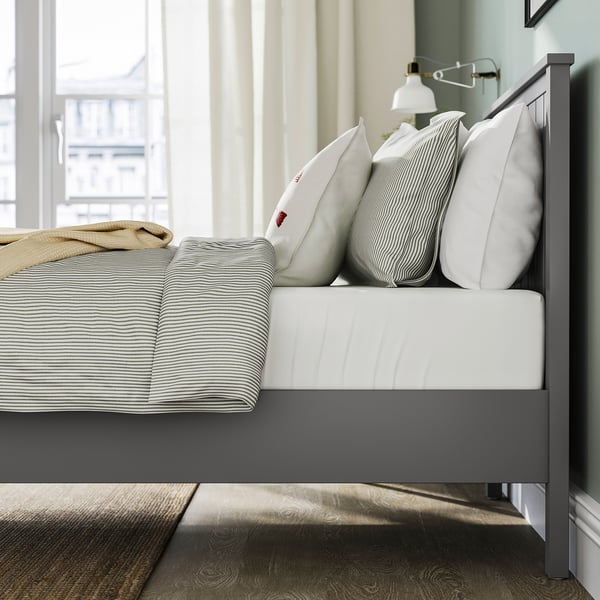 Neat bed with striped pillows, beige blanket, and grey headboard. Underbed space for storage.