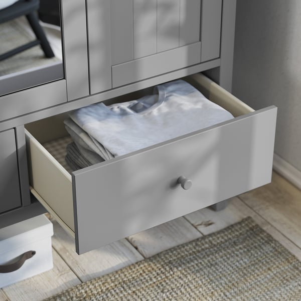 Open grey wooden drawer from gullberg series, holding folded clothes on a rug.
