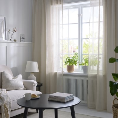 Beige HÄLLEBRÄCKA curtains on large window, airy living room.