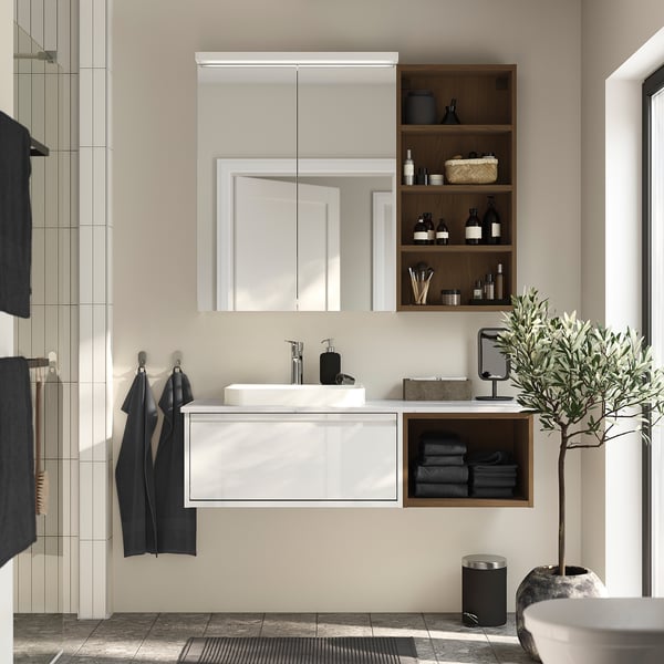 Modern bathroom with HAGAÅN white cabinet, large mirror above and open shelves. Black accents and a plant on the side. Clean and minimalist design.