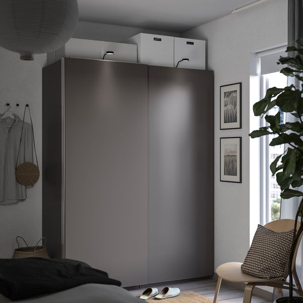 Modern bedroom with grey HASVIK wardrobe, white boxes, striped shirt, and wooden chair near a window.