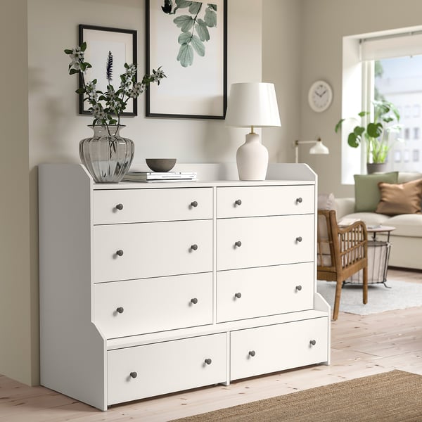 HAUGA chest with 6 drawers in well-lit room, silver handles, decorative top, next to artwork.