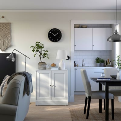 Modern open-concept home with white HAVSTA cabinet, grey chair, plant, lamp, clock, and dining area.