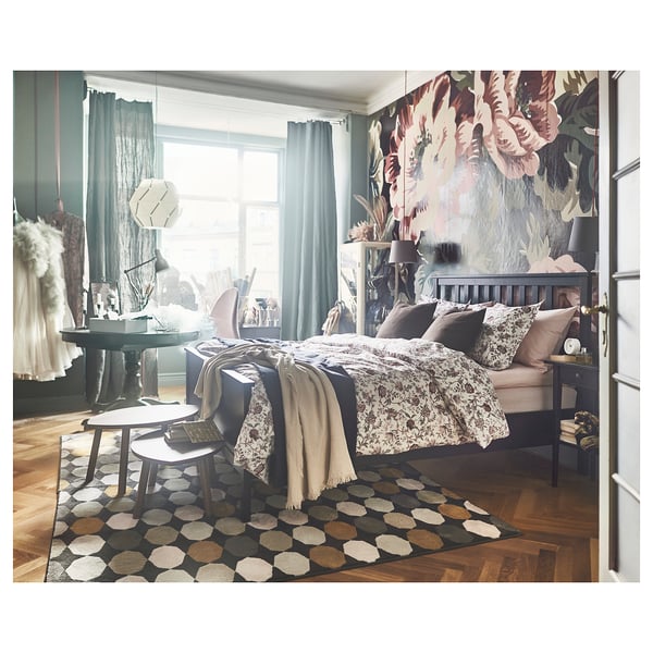 Modern bedroom with HEMNES bed, floral wallpaper, patterned rug, and cosy textiles.