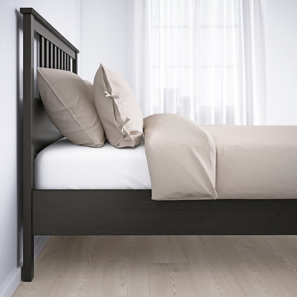 Minimalist bed with beige pillows and blanket, dark wood headboard, slatted floors.