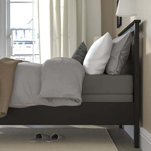 Made bed with grey sheets and pillows, dark wood frame, slatted base, grey slippers.