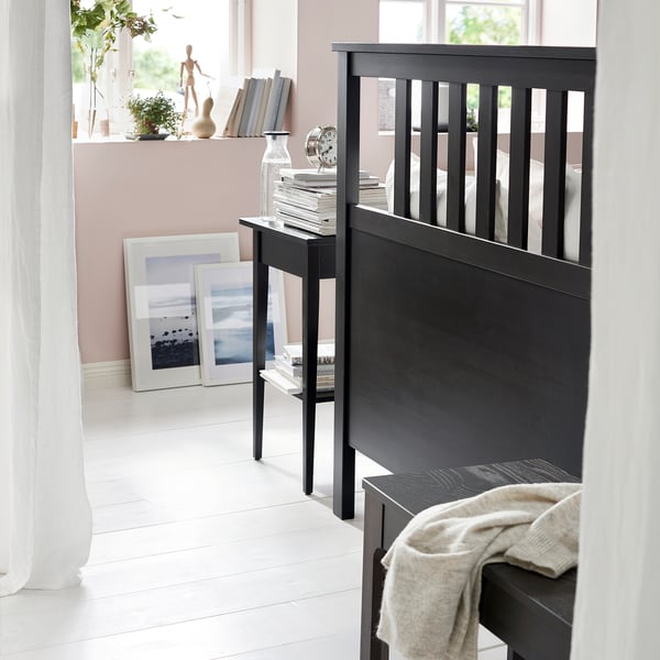 Black wooden bed with white walls, light-colored floor, and decorated shelves.