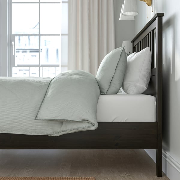 Bedroom with HEMNES wooden bed frame, white mattress, light green linens, and large window with curtains.