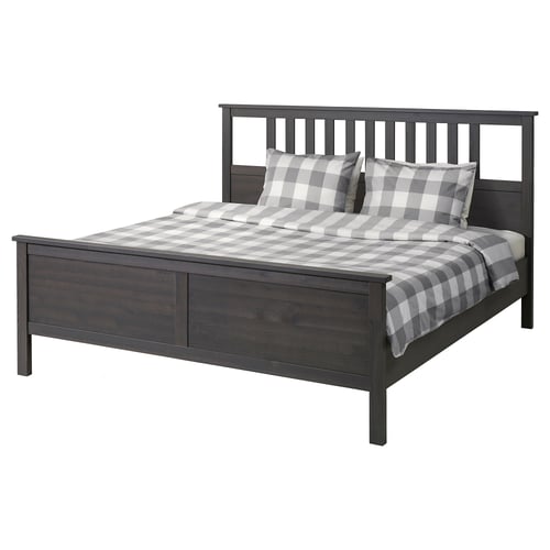 Dark brown wooden bed with grey and white chequered bedding and pillows. Square headboard and footboard, simple modern design.