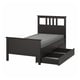 A black single HEMNES bed with underside storage and a grey mattress. The bed is made of solid pine wood.