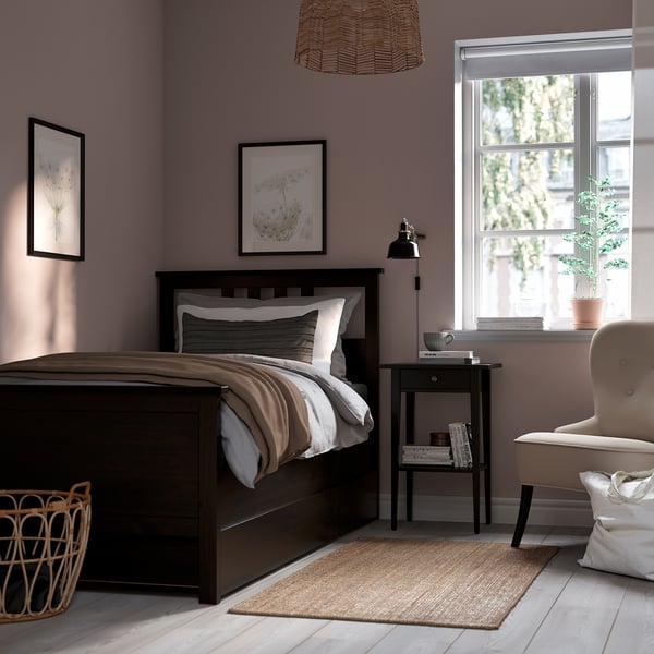 HEMNES bed in cosy mauve room, two prints, chair, side table with lamp, books, and plant.