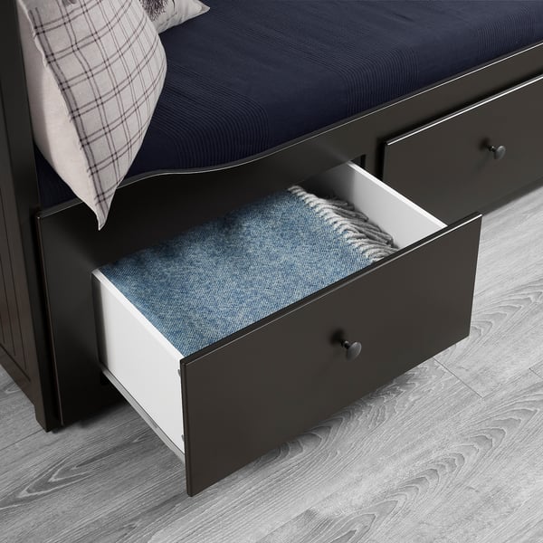 Open bedside drawer reveals neatly folded blankets. Dark wood drawer against grey floor, part of modern bed.