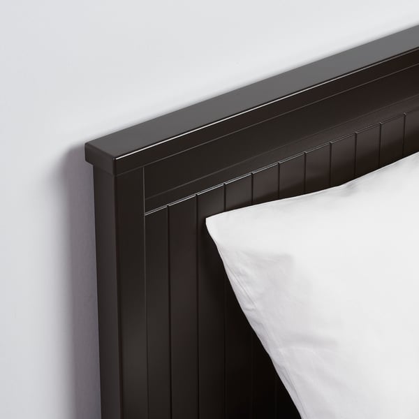 Black wooden bed frame, sleek design, smooth finish, single white pillow atop crisp white bedding.
