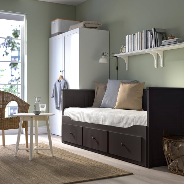 Modern bedroom with grey HEMNES day-bed, white bedding, brown pillows. Under wall shelf with books and clock, next to white wardrobe.