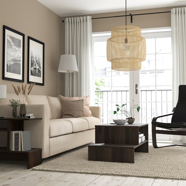 Minimalist living room with beige sofa, wooden coffee table, black armchair, large window, and pendant lamp. Beige walls and neutral rug.